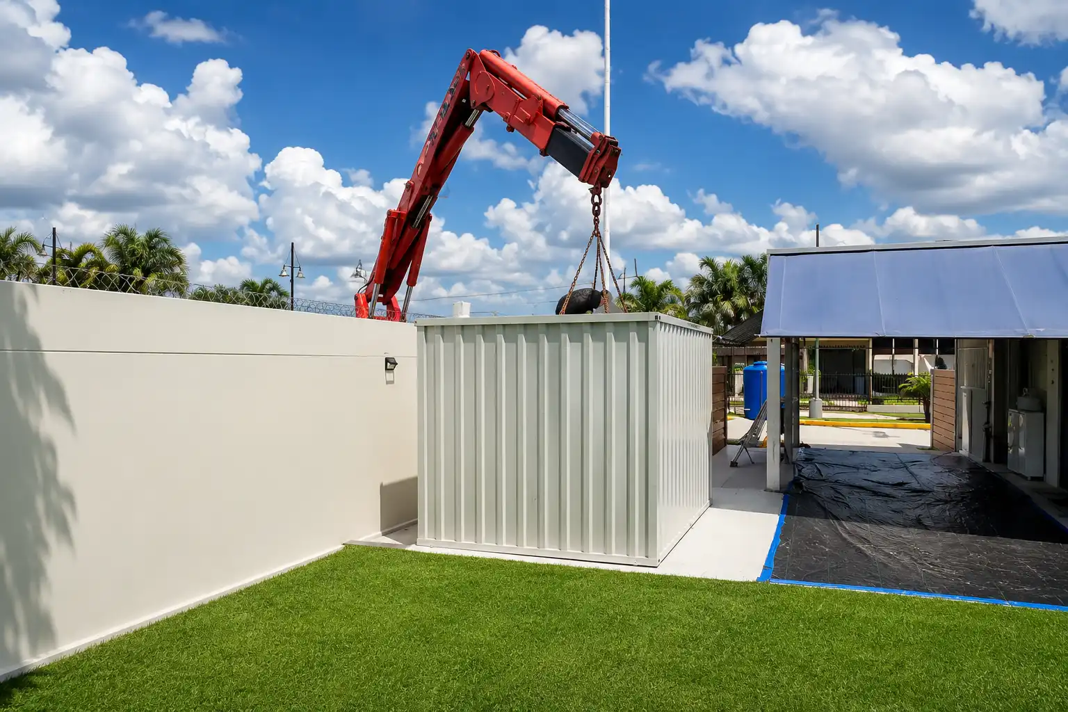 Portable steel storage container being installed with a crane at a commercial facility under a bright blue sky.